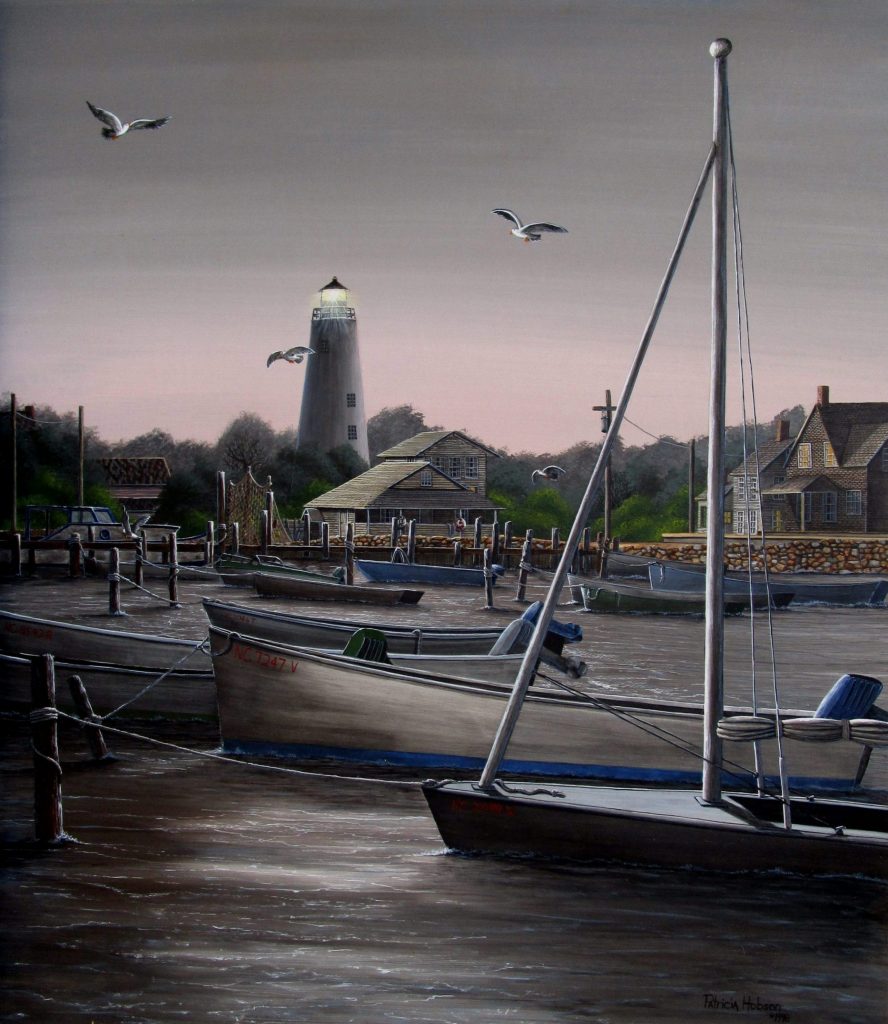 Nautical art print features a romantic evening view of the Ocracoke Lighthouse and village as scene through the boats from the water on the coast of North Carolina.