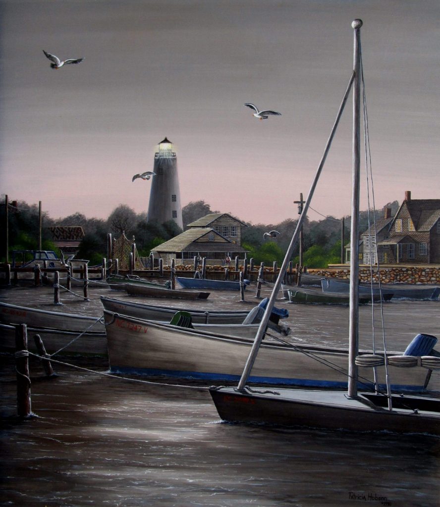 This is a romantic evening view of the Ocracoke Lighthouse and village as scene through the boats from the water on the coast of North Carolina.